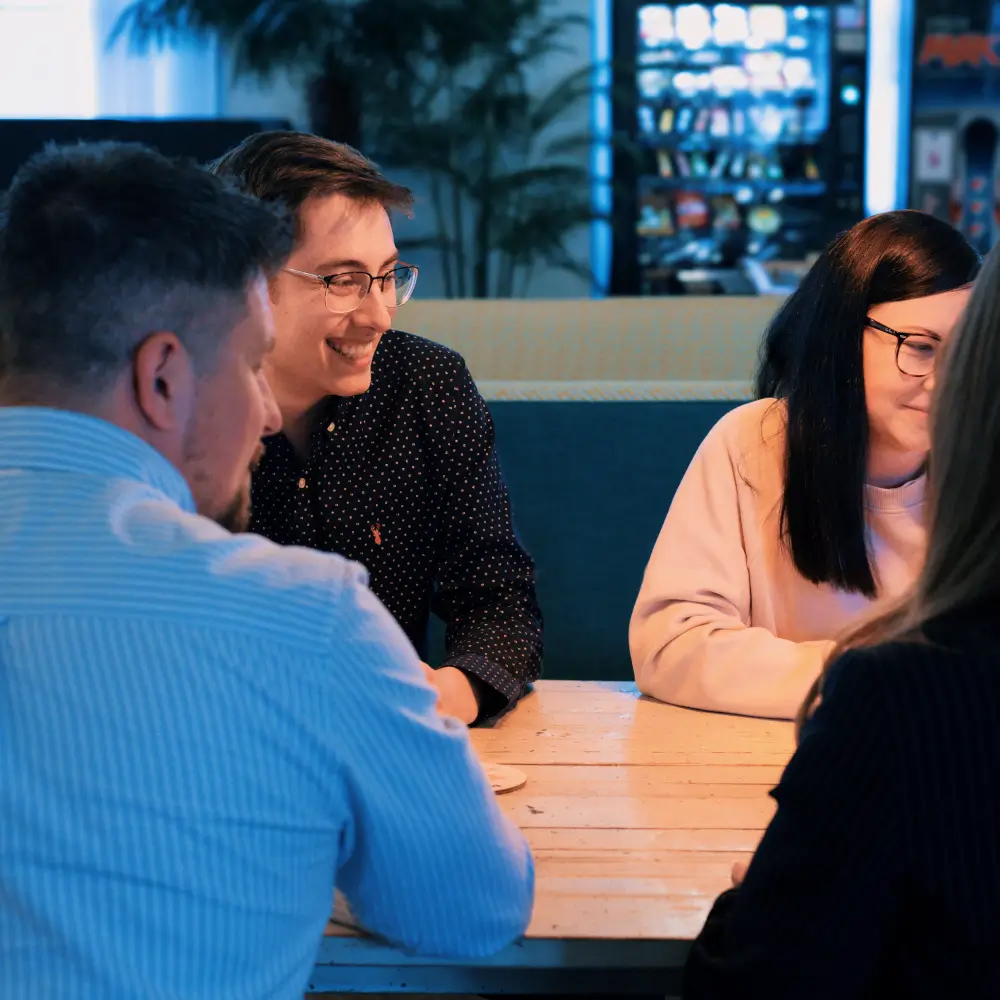 lgb-team-support two male and two female members of staff sat around a table smiling and looking at something off camera.